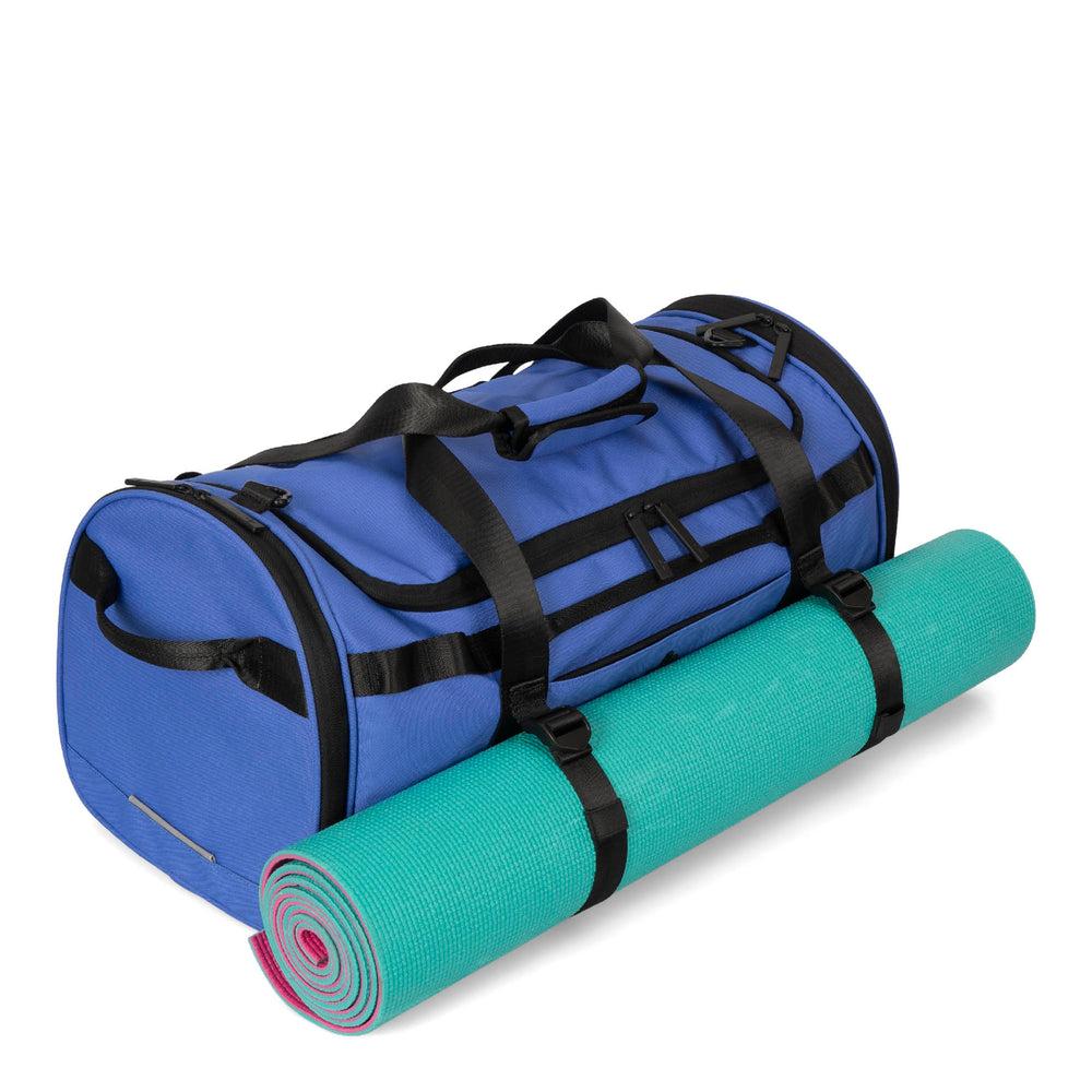 Angle view of a blue duffle bag called Banff designed by Tracker showing its shoulder strap, top handles, front tracker logo, a turqoise-coloured yoga mat, and multiple zippers.