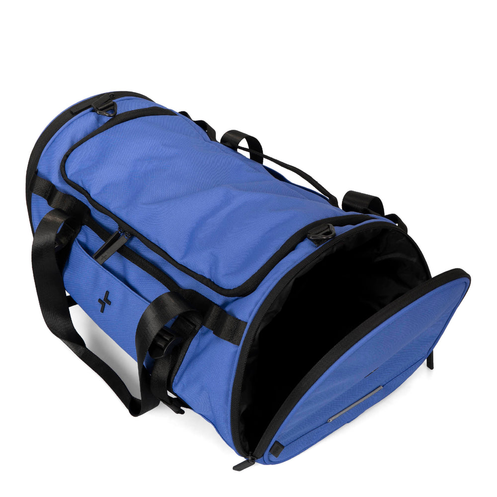 Angle view of a blue duffle bag called Banff designed by Tracker showing its open side shoe pocket, top handles, front tracker logo, and multiple zippers.