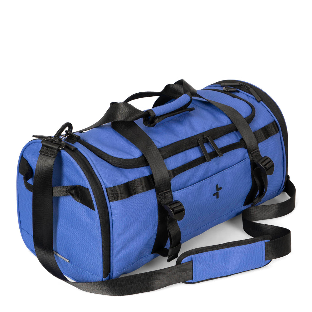 Angle view of a blue duffle bag called Banff designed by Tracker showing its shoulder strap, top handles, front tracker logo, and multiple zippers.