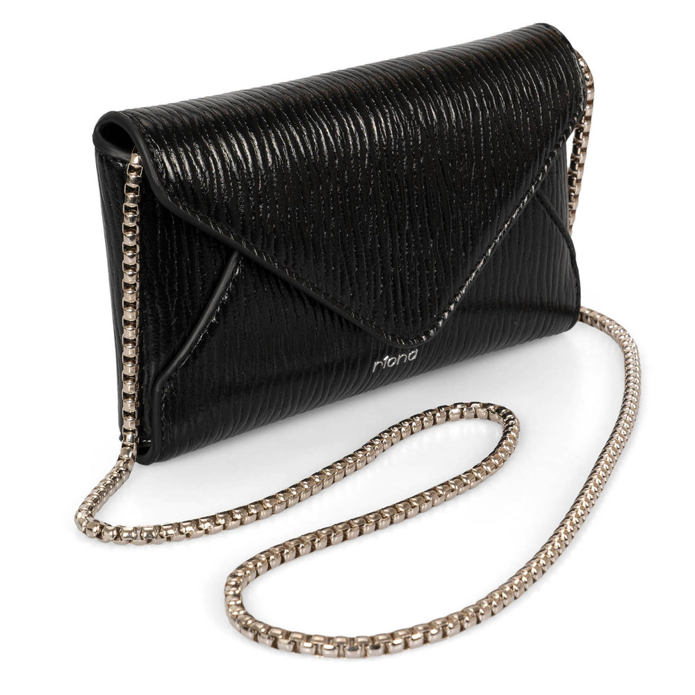 Angle view of black glossy crossbody bag called Evening in an envelopy style designed by Riona, showcasing its chain strap and shiney textured PU look.